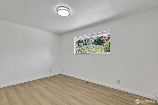 empty room featuring baseboards, visible vents, and light wood finished floors