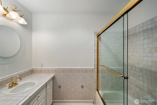 full bath with wainscoting, combined bath / shower with glass door, vanity, and tile walls