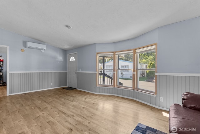 11519 21st Ave E Unit 84, Tacoma, WA 98445 - unfurnished living room with wainscoting, a wall unit AC, a textured ceiling, and wood finished floors