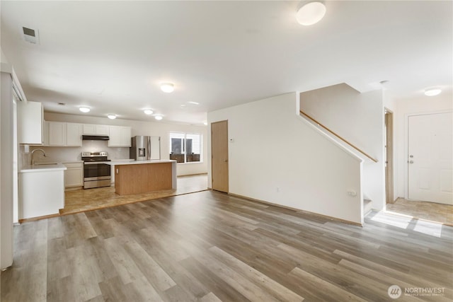 unfurnished living room with stairway, a sink, and light wood finished floors