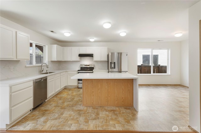 kitchen featuring white cabinets, a sink, under cabinet range hood, a kitchen island, and appliances with stainless steel finishes