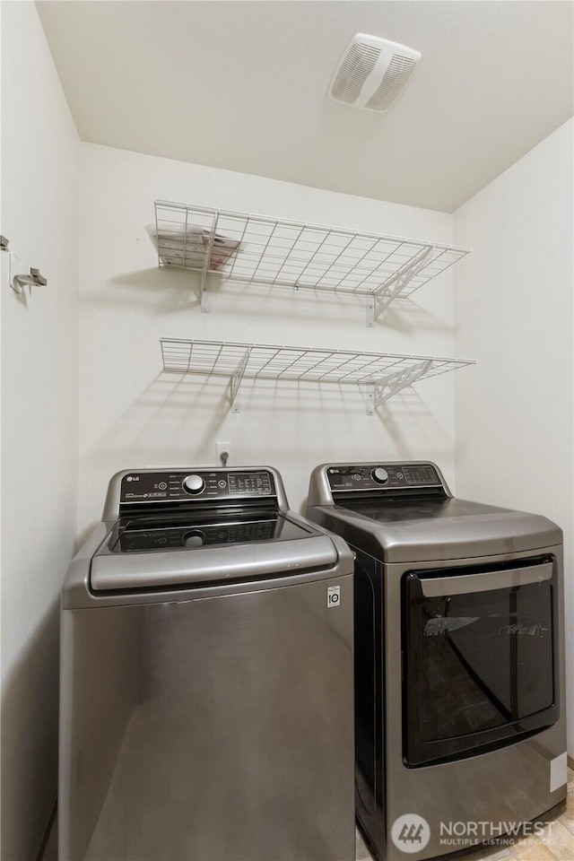 washroom featuring washing machine and clothes dryer, visible vents, and laundry area