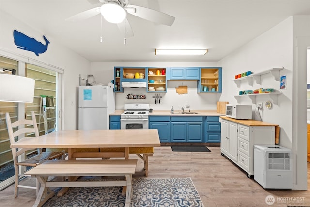 kitchen featuring a sink, white appliances, blue cabinetry, open shelves, and under cabinet range hood