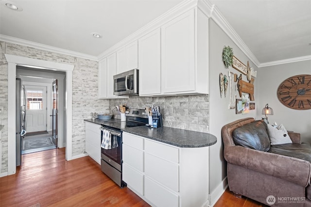 kitchen with crown molding, light wood finished floors, stainless steel appliances, open floor plan, and white cabinetry