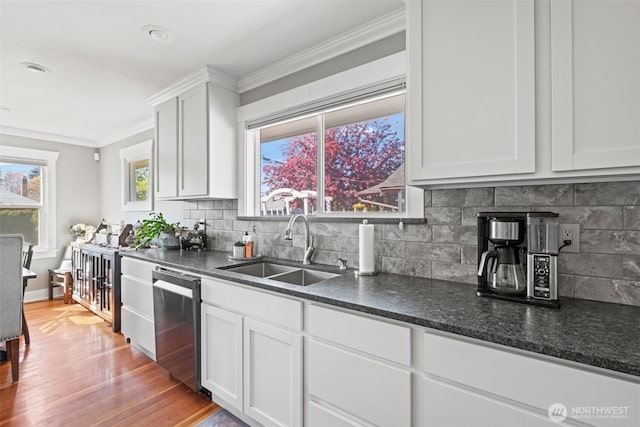kitchen featuring crown molding, tasteful backsplash, dishwasher, a sink, and light wood finished floors