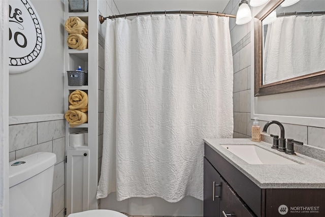bathroom with wainscoting, tile walls, vanity, and toilet