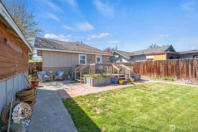 rear view of property with a shingled roof, a wooden deck, a fenced backyard, a lawn, and a patio
