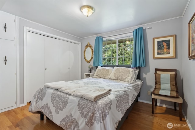 bedroom with crown molding, baseboards, a closet, and wood finished floors