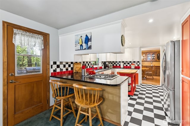 kitchen featuring white cabinets, appliances with stainless steel finishes, tile patterned floors, a peninsula, and decorative backsplash