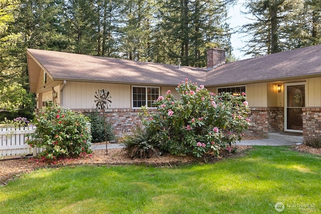 ranch-style home featuring brick siding, a chimney, roof with shingles, and a front lawn