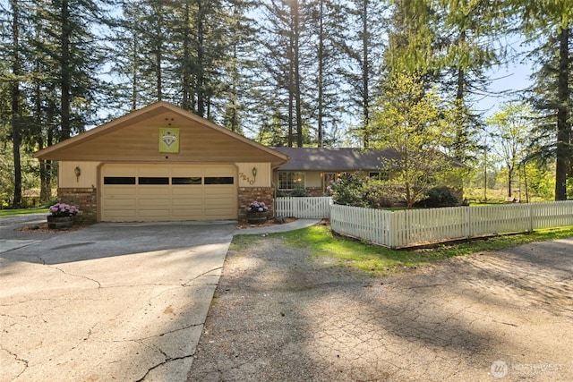 view of front facade featuring brick siding, an attached garage, a fenced front yard, and aphalt driveway