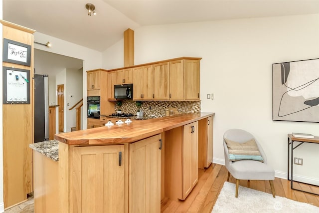 kitchen featuring lofted ceiling, light wood finished floors, light brown cabinetry, backsplash, and black appliances