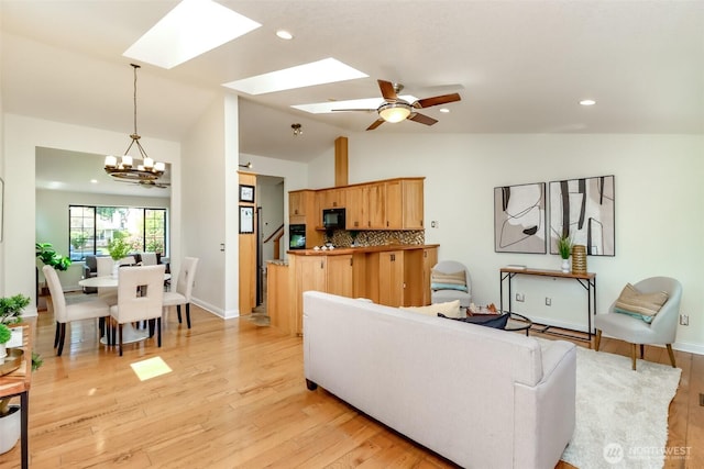 living area featuring vaulted ceiling with skylight, light wood finished floors, baseboards, and ceiling fan with notable chandelier