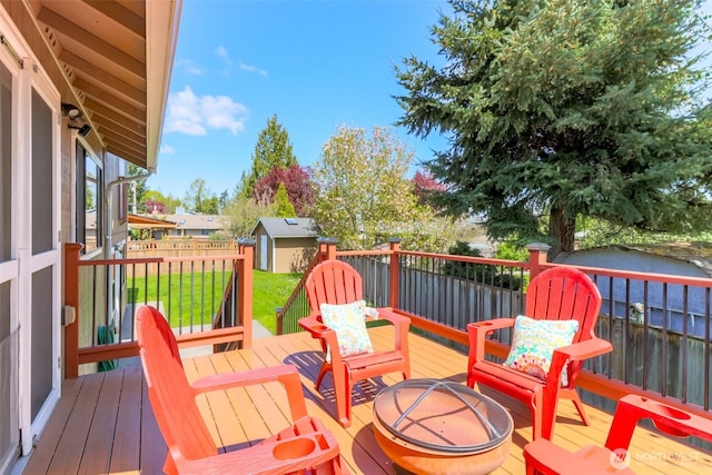 wooden deck with fence, a storage shed, an outdoor structure, a lawn, and a fire pit