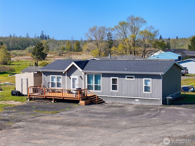 view of front of home with a wooden deck, roof with shingles, an outbuilding, and a shed