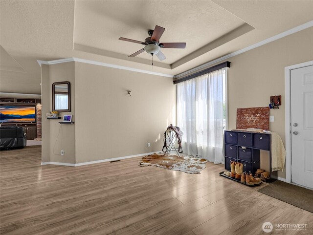 interior space with a raised ceiling, wood finished floors, a ceiling fan, and baseboards