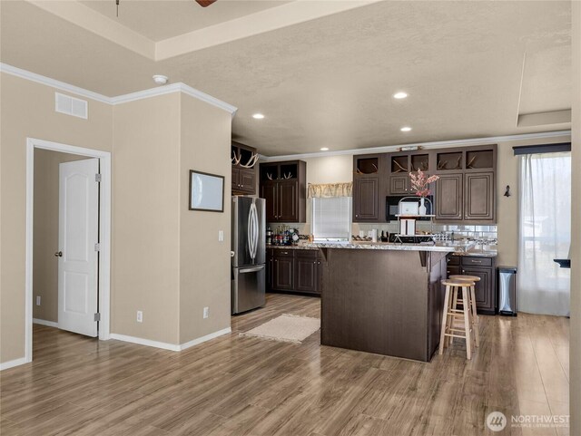 kitchen with a kitchen breakfast bar, tasteful backsplash, visible vents, freestanding refrigerator, and dark brown cabinetry