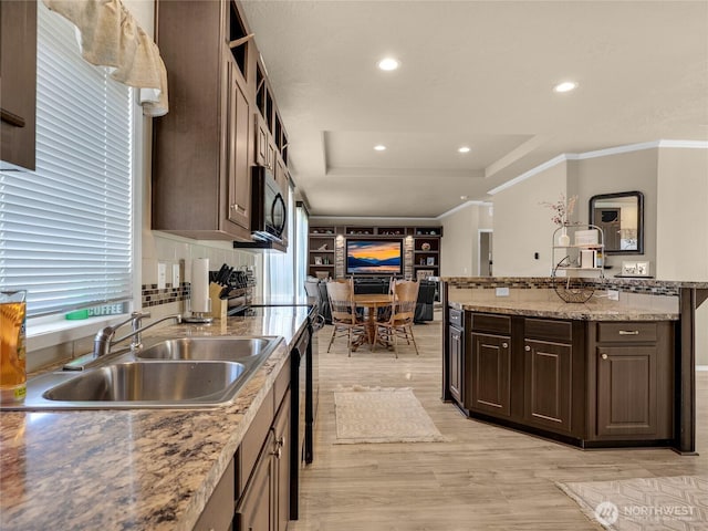 kitchen featuring dark brown cabinets, a sink, black microwave, light wood-style floors, and a tray ceiling