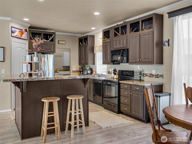 kitchen featuring black appliances, light wood-style floors, a breakfast bar, backsplash, and ornamental molding