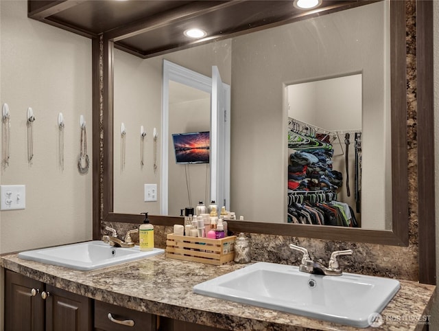 bathroom featuring a spacious closet, a sink, and double vanity