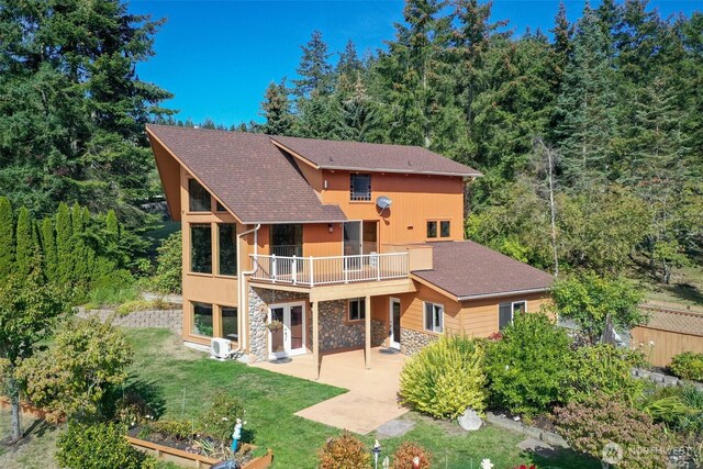 rear view of house with a patio, stone siding, a yard, and roof with shingles