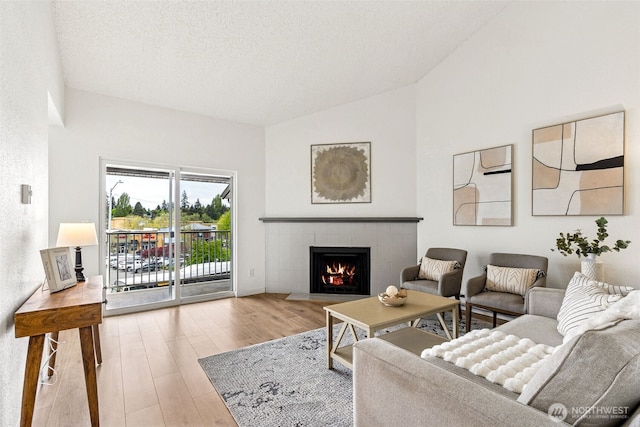 living room with a textured ceiling, a fireplace, wood finished floors, and lofted ceiling