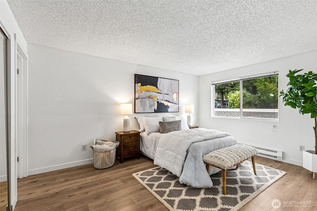 bedroom featuring baseboards, a textured ceiling, baseboard heating, and wood finished floors