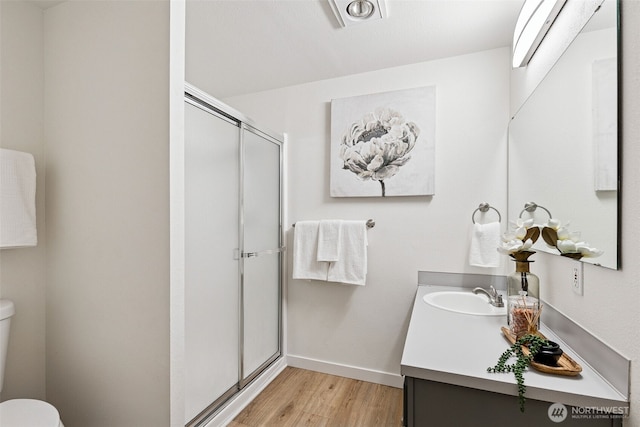 bathroom featuring vanity, wood finished floors, toilet, baseboards, and a stall shower