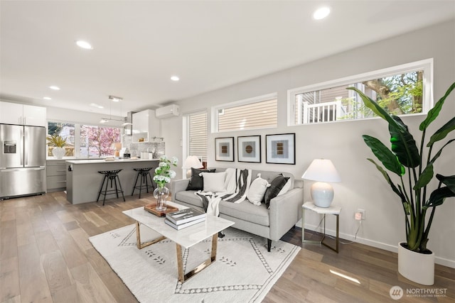 living room featuring recessed lighting, a wall mounted AC, light wood finished floors, and baseboards