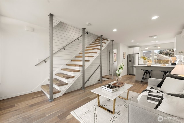 living room featuring baseboards, recessed lighting, light wood-style floors, and stairway