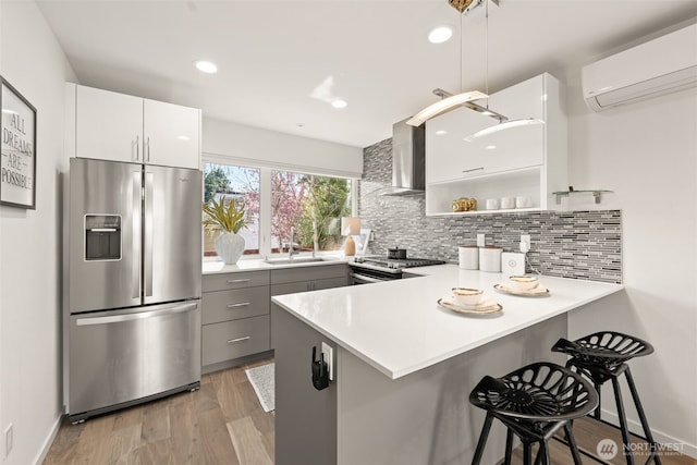 kitchen with wall chimney range hood, a sink, a wall mounted AC, stainless steel appliances, and gray cabinetry