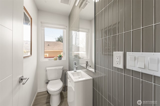 half bathroom with wood finished floors, visible vents, toilet, vanity, and baseboards