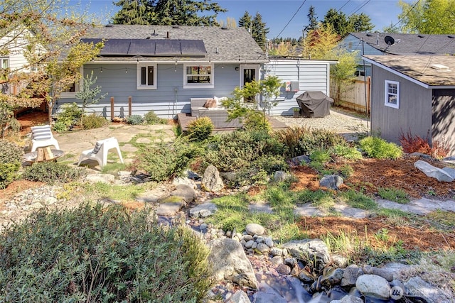 rear view of property featuring roof mounted solar panels, a shingled roof, and fence