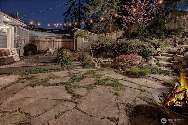 yard at twilight featuring an outdoor structure, a fenced backyard, a storage shed, and a deck