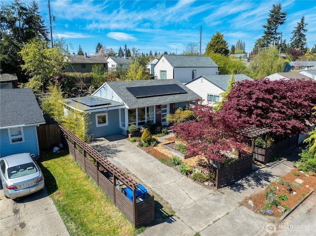 view of front of property with a shingled roof, roof mounted solar panels, fence, a garden, and a residential view