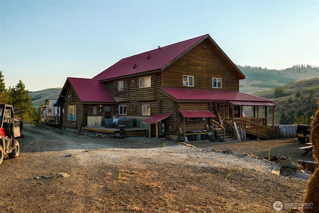back of property featuring a deck with mountain view, a porch, metal roof, and log siding