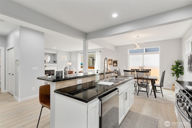 kitchen with appliances with stainless steel finishes, a sink, light wood-type flooring, an island with sink, and white cabinets
