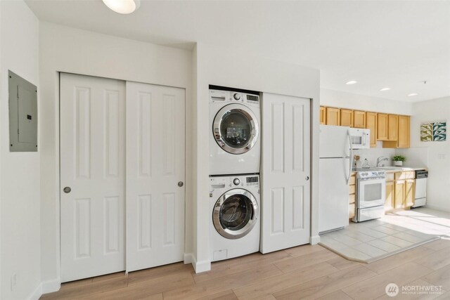 washroom with a sink, electric panel, light wood finished floors, stacked washer and dryer, and laundry area