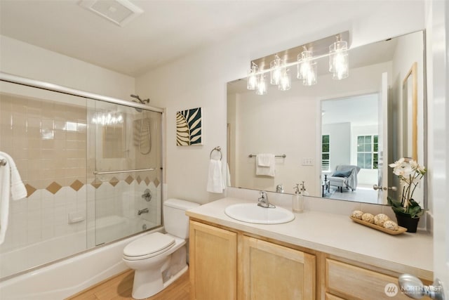 bathroom with bath / shower combo with glass door, toilet, vanity, and wood finished floors
