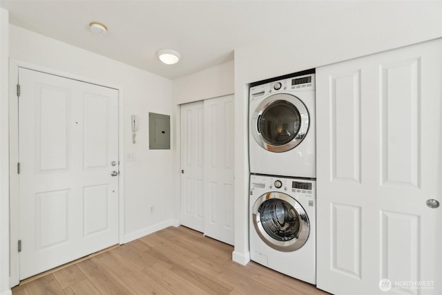 laundry area featuring light wood finished floors, laundry area, stacked washing maching and dryer, electric panel, and baseboards