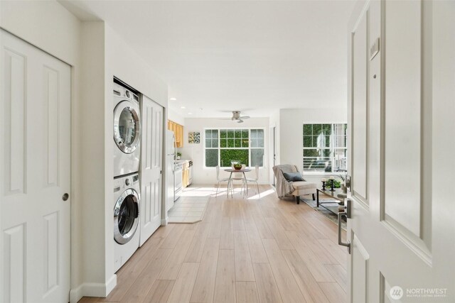 laundry area with a ceiling fan, stacked washing maching and dryer, light wood finished floors, baseboards, and laundry area