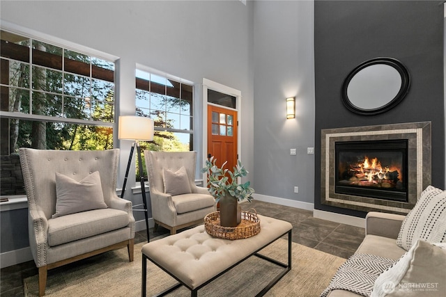 living room with baseboards, a tiled fireplace, and a high ceiling