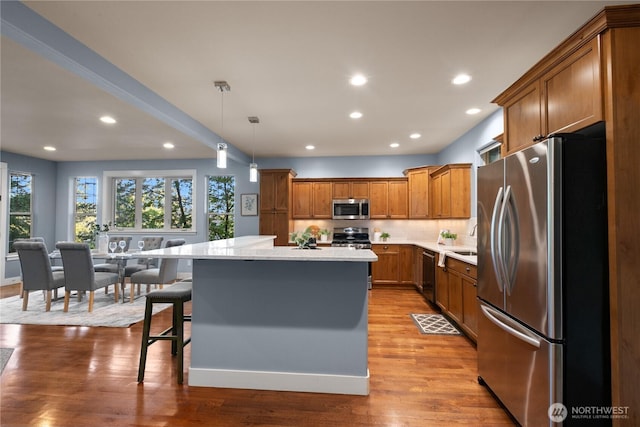 kitchen with appliances with stainless steel finishes, a center island, brown cabinetry, recessed lighting, and a breakfast bar area