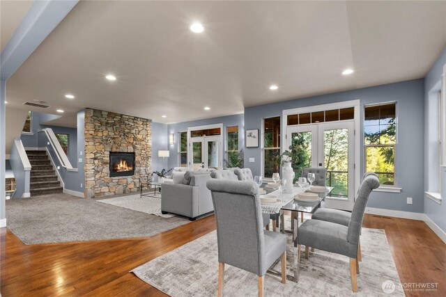 dining area featuring french doors, stairway, a stone fireplace, wood finished floors, and recessed lighting