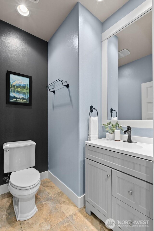bathroom with baseboards, toilet, stone tile flooring, and vanity