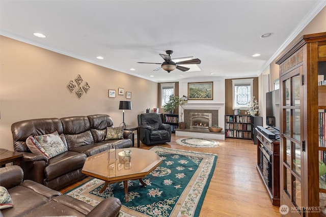living room with ceiling fan, a warm lit fireplace, crown molding, and light wood finished floors