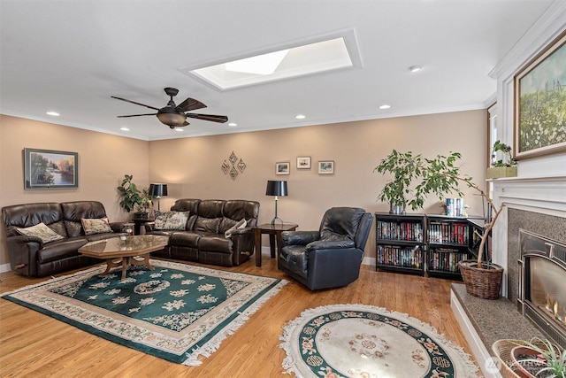 living room featuring crown molding, wood finished floors, a skylight, ceiling fan, and a fireplace