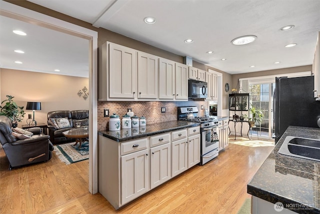 kitchen with white cabinets, light wood finished floors, backsplash, black appliances, and open floor plan