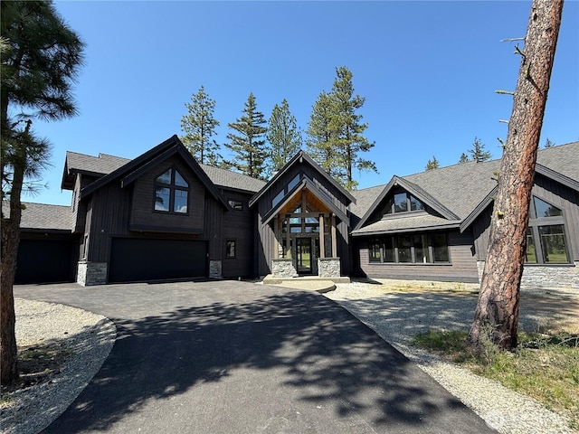 view of front of house featuring driveway, stone siding, a shingled roof, and a garage