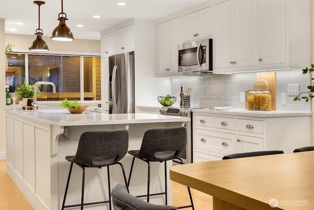 kitchen with white cabinets, a kitchen breakfast bar, stainless steel appliances, a kitchen island, and decorative backsplash